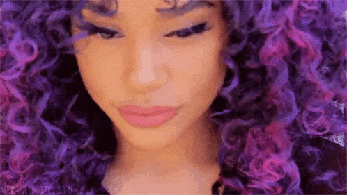 a close up of a woman 's face with purple hair .