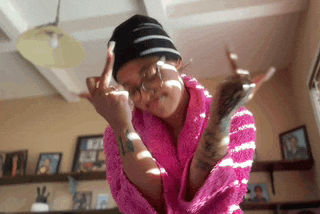 a woman wearing a pink robe and a black hat is giving the middle finger