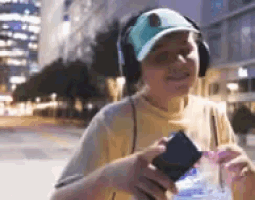 a person wearing headphones and a hat is holding a cell phone .