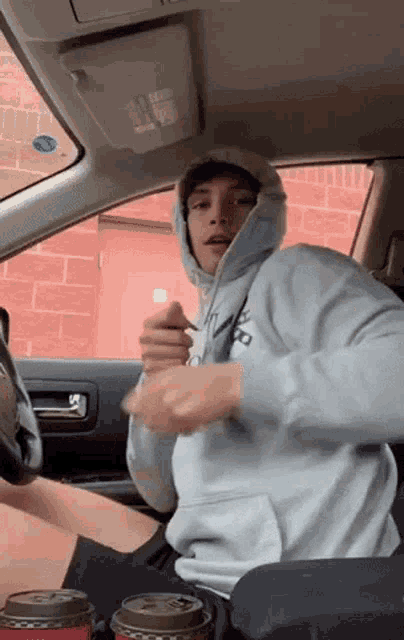 a man in a hoodie is sitting in the driver 's seat of a car .