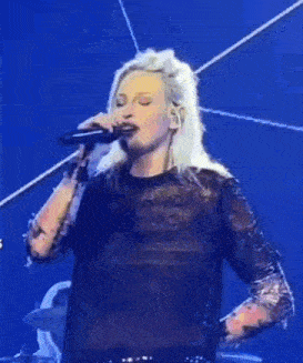a woman is standing on a stage wearing a black lace top and holding a microphone .