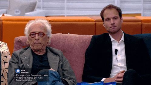 two men are sitting on a couch and one of them has a hashtag that starts with the letter g.