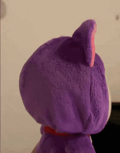 a close up of a purple stuffed animal with a red collar
