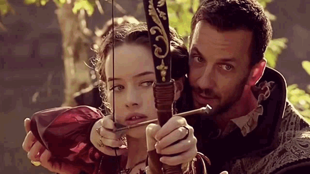 a man is holding a bow and arrow next to a woman who is holding a bow and arrow