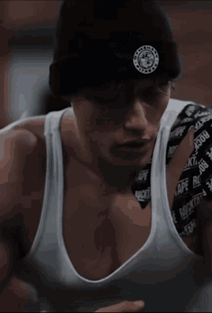 a man wearing a black beanie and a white tank top has tape on his shoulder that says ' tape big '