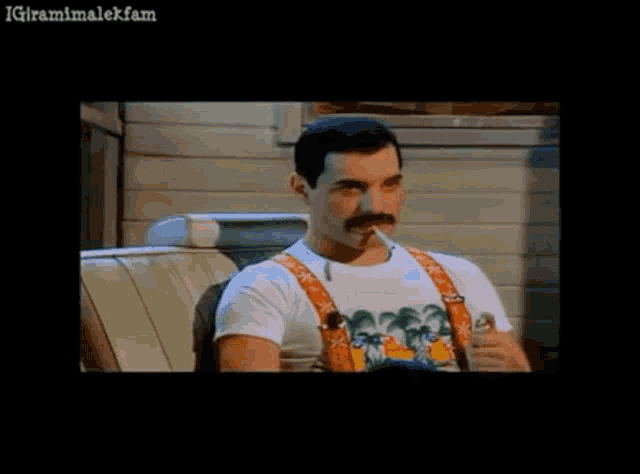 a man with a mustache is smoking a cigarette while sitting in a chair .