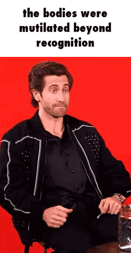 a man in a black jacket is sitting at a table with a glass of whiskey in front of a red background .