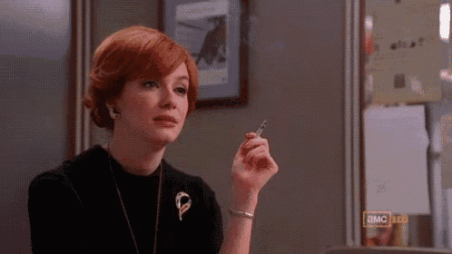 a woman with red hair is smoking a cigarette in a room with a sign that says ' bmc ' on it