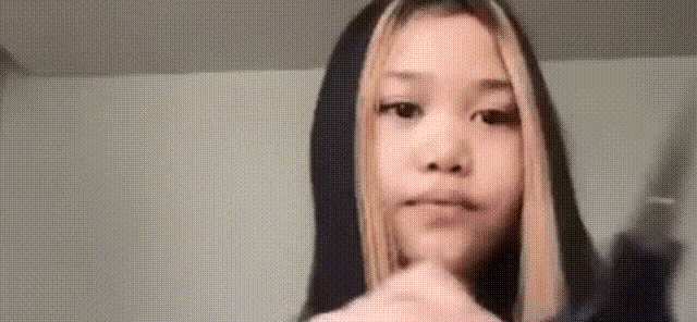 a girl in a black hoodie is holding a knife in her hand and making a funny face .