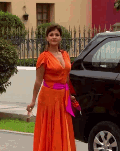 a woman in an orange dress is standing next to a black car
