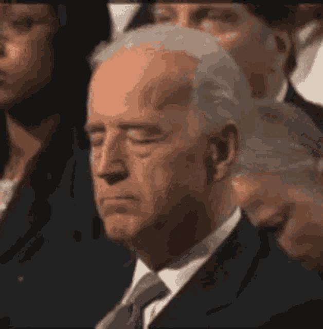 a man in a suit and tie is sitting with his eyes closed in a crowd .