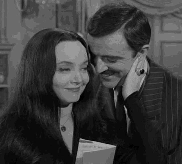 a man and a woman are looking at each other in a black and white photo . the man is holding a book .