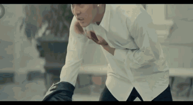 a man in a white shirt and black pants holds his chest