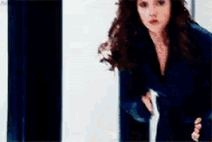 a woman in a black suit is standing in front of a white wall and a black curtain ..