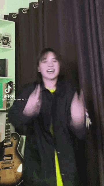 a girl wearing a black jacket and a yellow shirt is giving the middle finger