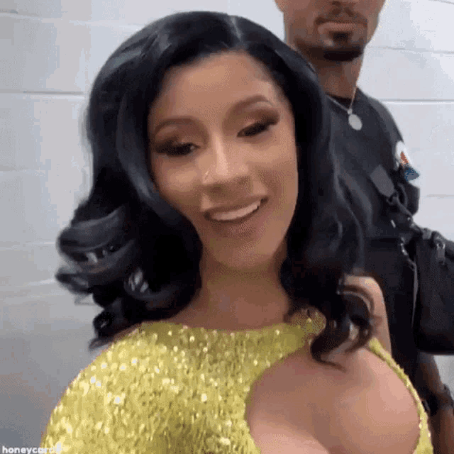 cardi b is wearing a yellow dress and smiling for the camera .