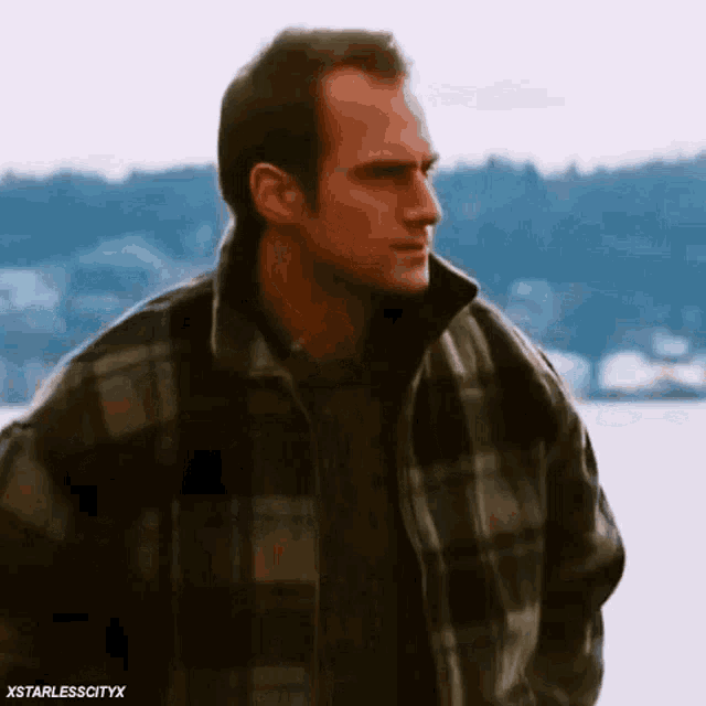 a man wearing a plaid jacket is standing in front of a body of water .