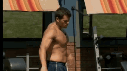 a shirtless man in blue shorts is standing in front of a brick building .