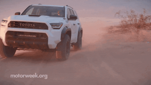 a white toyota is driving on a dirt road in the desert