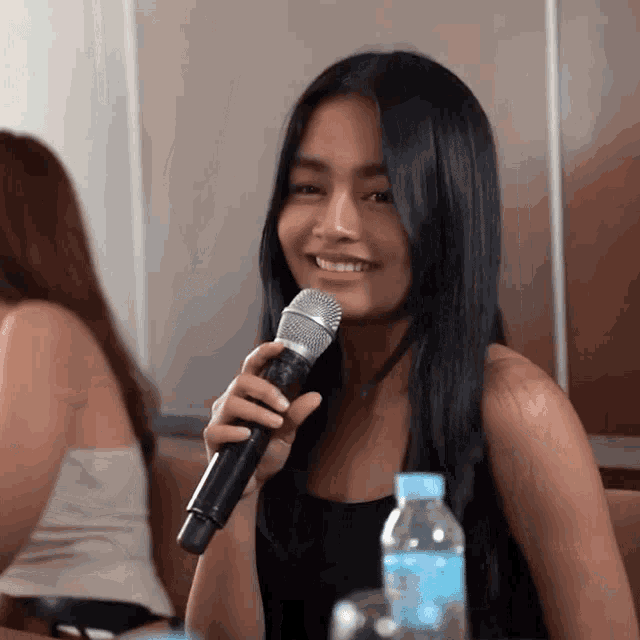 a woman is holding a microphone and smiling in front of a bottle of water