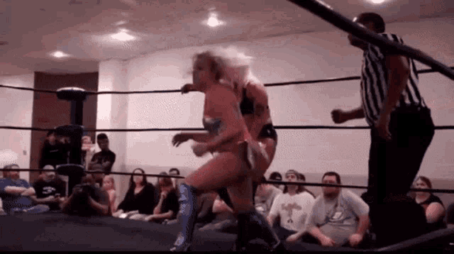 two women are wrestling in a ring while a referee looks on .