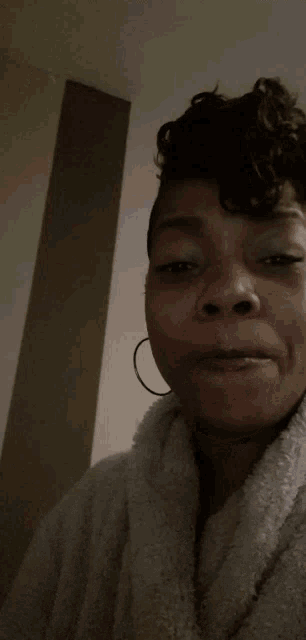 a woman wearing a white robe and hoop earrings is making a face
