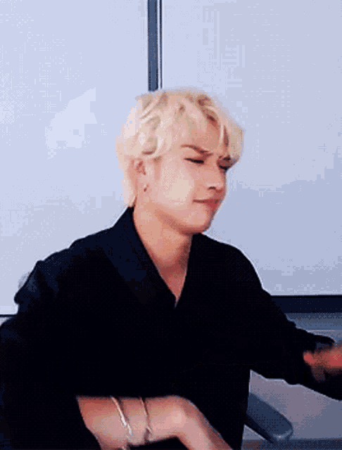 a man with blonde hair wearing a black shirt is making a funny face
