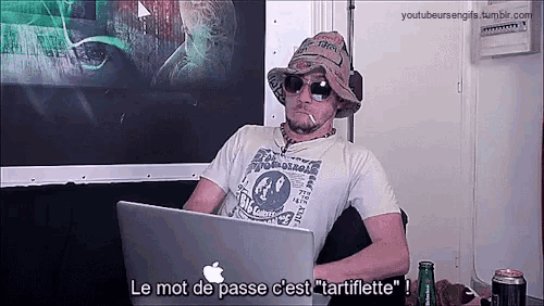 a man wearing a hat and sunglasses is sitting in front of an apple laptop ..