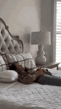 a woman is laying on a bed with plaid pillows and a lamp