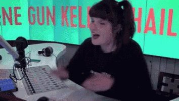 a woman is singing into a microphone in front of a sign that says " ne gun kelly hail "