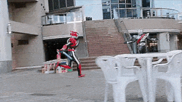 a man in a superhero costume is standing in front of a table and chairs .