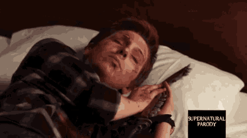 a man in a plaid shirt is laying in bed with a supernatural parody sign next to him