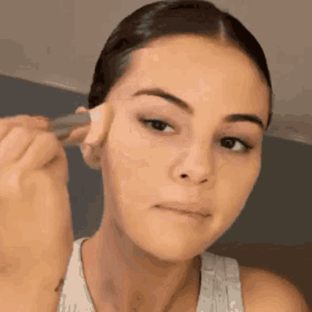 a woman is applying makeup to her face with a sponge .