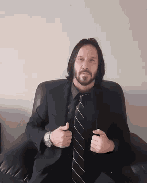 a man in a suit and tie is sitting in a chair with his hands folded