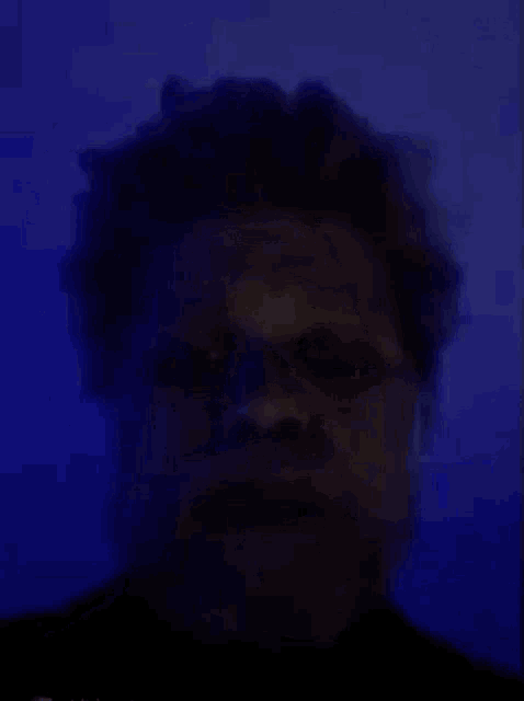 a man with a beard is looking at the camera in a dark room .
