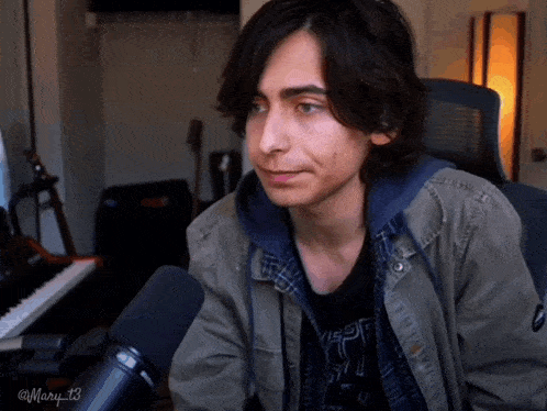 a young man sitting in front of a microphone with the name mary 13 on the bottom right