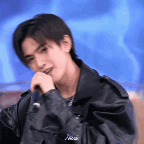 a young man wearing a leather jacket is singing into a microphone