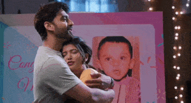 a man and a woman are hugging in front of a picture of a child .