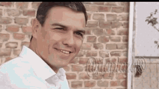 a man is smiling in front of a brick wall and looking at the camera .