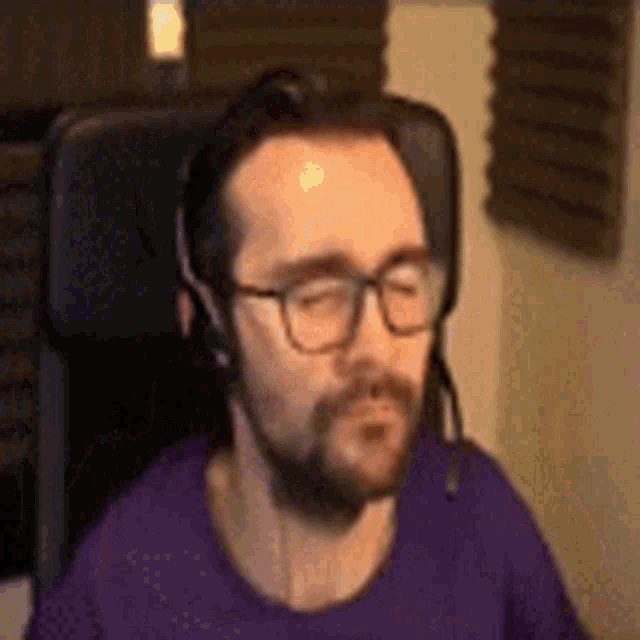 a man with a beard wearing headphones and glasses is sitting in a chair .