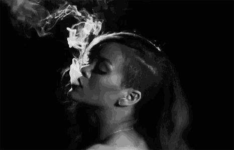 a woman with a shaved head is smoking a cigarette and smoke is coming out of her mouth .