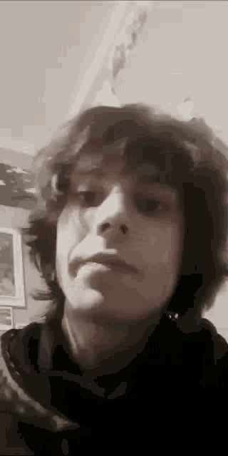 a young man with long hair is looking at the camera in a room .
