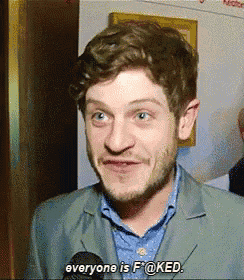 a man in a suit is talking into a microphone and saying everyone is f @ ked