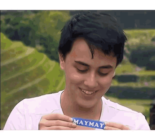 a young man in a white shirt is smiling and holding a maymay bar