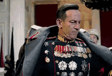 a man in a military uniform with medals on his jacket is standing in front of a group of people .