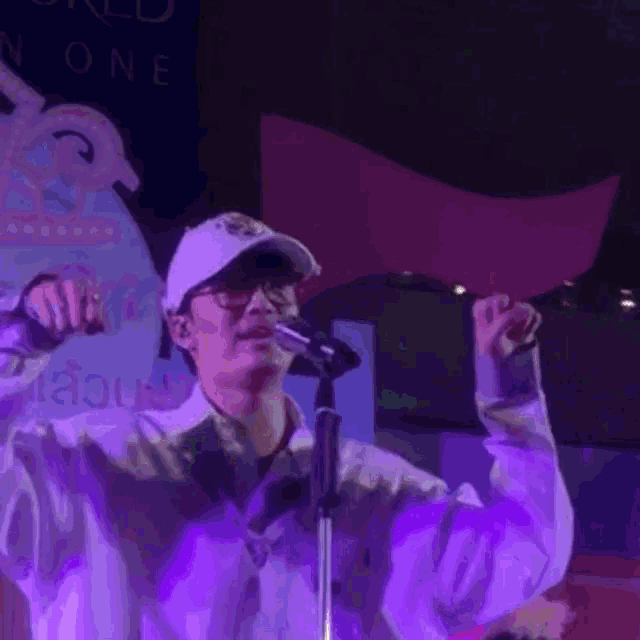 a man is singing into a microphone while wearing a hat and glasses