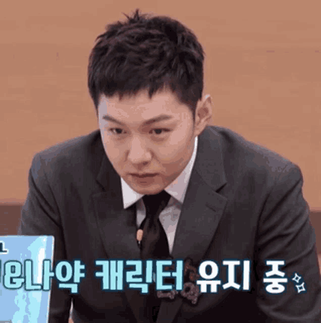 a man in a suit and tie is sitting in front of a laptop with korean writing on the screen