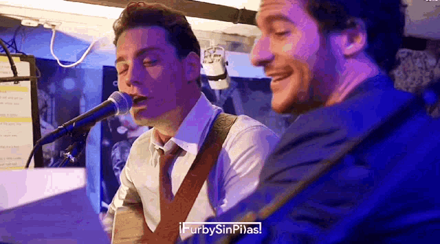 a man singing into a microphone next to another man playing a piano