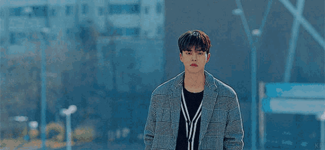 a young man wearing a plaid jacket and a black sweater is standing in front of a building .