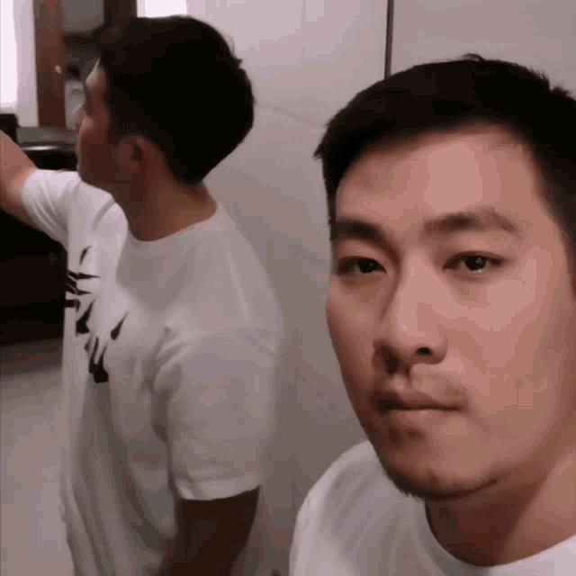 a man in a white shirt with the word nike on it looks at himself in a mirror